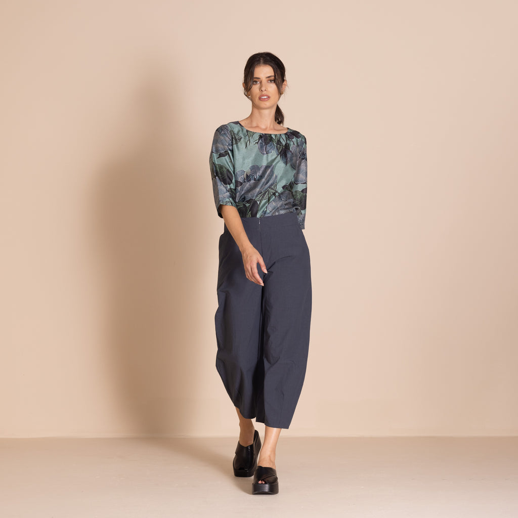 Woman wearing a floral top and dark pants against a beige background