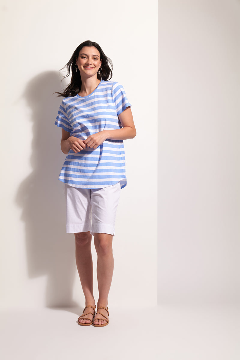 Woman wearing a blue and white striped shirt and white shorts against a plain background
